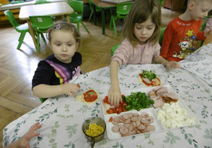 Dwie dziewczynki nakładają dodatki na ciasto.