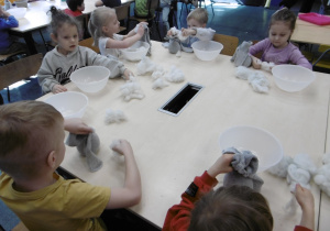 Dzieci siedzą przy stole i wykonują prace techniczne.