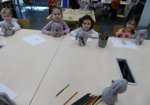 Czworo dzieci siedzi przy stole i w ręku trzyma wykonane maskotki.