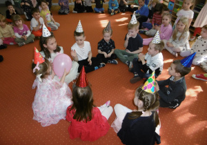 Dzieci siedzą w kole i podają sobie balon.