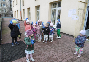 Dzieci stoją na tarasie przedszkola.