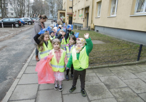 Grupa dzieci stoi na chodniku obok budynku mieszkalnego.
