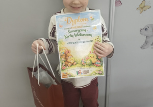 Chłopiec stoi z dyplomem w ręku.