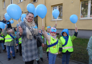 Nauczycielka i dzieci stoją przy budynku przedszkolnym