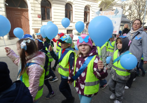 Grupa dzieci idzie razem w marszu i trzyma niebieskie balony.