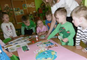 Kolejna grupa dzieci wspólnie nakleja papierowe elementy.