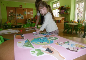 Nauczycielka pomaga dziewczynce nakleić wybrany element.
