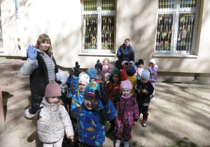 Grupa dzieci stoi razem przed oknami przedszkola.