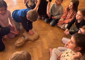 Dzieci siedzą w kole i uczą się sztucznego oddychania.