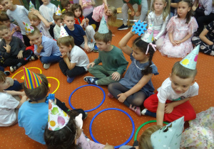 Kolejna grupa dzieci siedzi przy kolorowych obręczach.