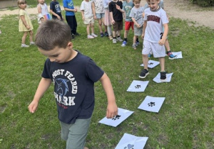 Dzieci chodzą po białych kartkach rozłożonych na trawie.