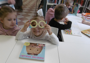 Dziewczynka trzyma papierowe okulary przy twarzy.