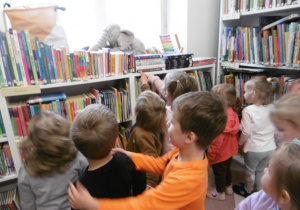 Grupa dzieci stoi przy półkach z książkami.