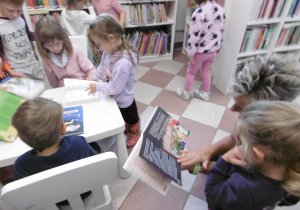 Grupa dzieci stoi przy białym stoliku z książkami.