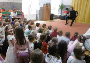 Dzieci siedzą na dywanie i słuchają muzyki.