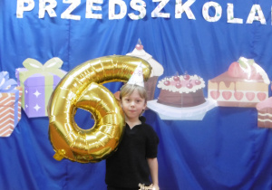 Jeden chłopiec stoi z balonem z cyfrą sześć.