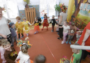 Grupa dzieci tańczy w kole na dywanie.