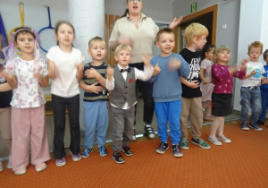 Grupa dzieci stoi obok siebie i wspólnie śpiewa.