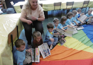 Dzieci siedzą w kole i trzymają gazety.