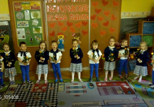 Tuptusie w ustawione w półkolu z różami w rękach podczas recytowania wiersza z okazji Dania Mamy i Taty