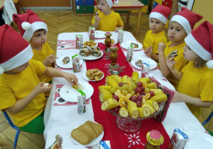 Smyki w żółtych koszulkach i czapeczkach mikołajowych przy stoliczkach