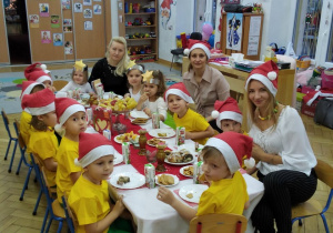 Smyki w żółtych koszulkach i czapeczkach mikołajowych przy stoliczkach