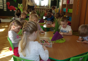 Tuptusie przy stoliczkach rysują kredkami ołówkowymi
