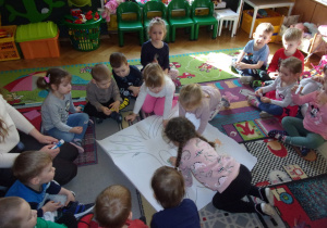 Tuptusie na dywanie przyklejają elemanty na białym arkuszu papieru