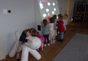 dziewczynka na plastikowym koniku, w tle dzieci przy tablicy interaktywnej