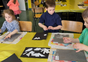 troje dzieci przy stole wykonuje pracę plastyczną z przygotowanego papieru
