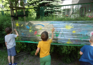 dzieci malują farbami plakatowymi na foliach rozwieszonych w ogrodzie przedszkolnym