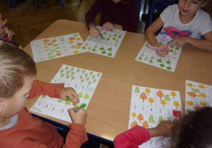 Juniorzy przy stolikach pzeliczają drzewa przedstawione na ilustracjach