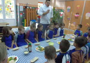 Juniorzy w fartuszkach przy stolikach przygotowują zapiekanki