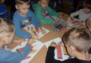 Juniorzy przy stolikach podpisują swoje prace
