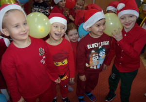 dzieci ubrane na czerwono w mikołajkowych czapeczkach podczas zabawy z balonami