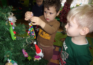 dwóch chłopców zawiesza na choince ozdoby choinkowe